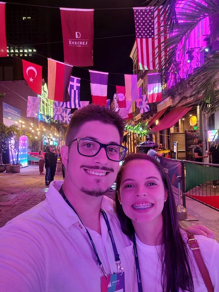 Caroline e Lucas numa rua com bandeiras no Rio de Janeiro